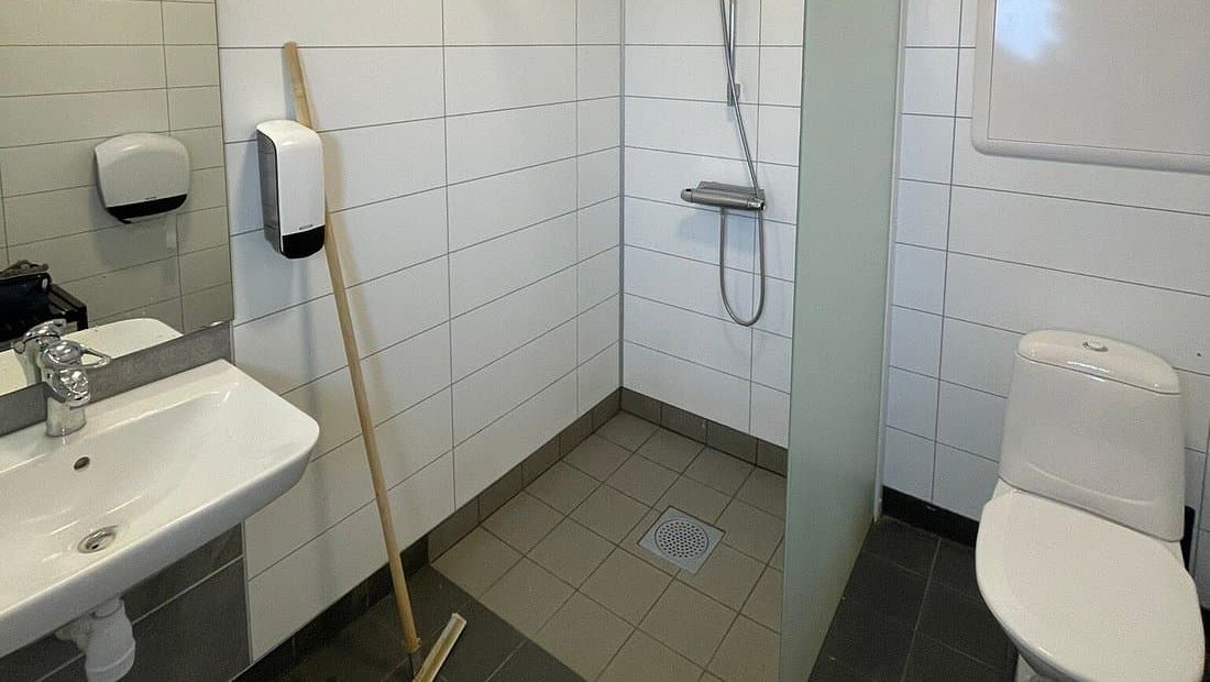 Lyst og moderne baderom med servant, dusj, toalett, såpedispenser og flislagt gulv og vegger.